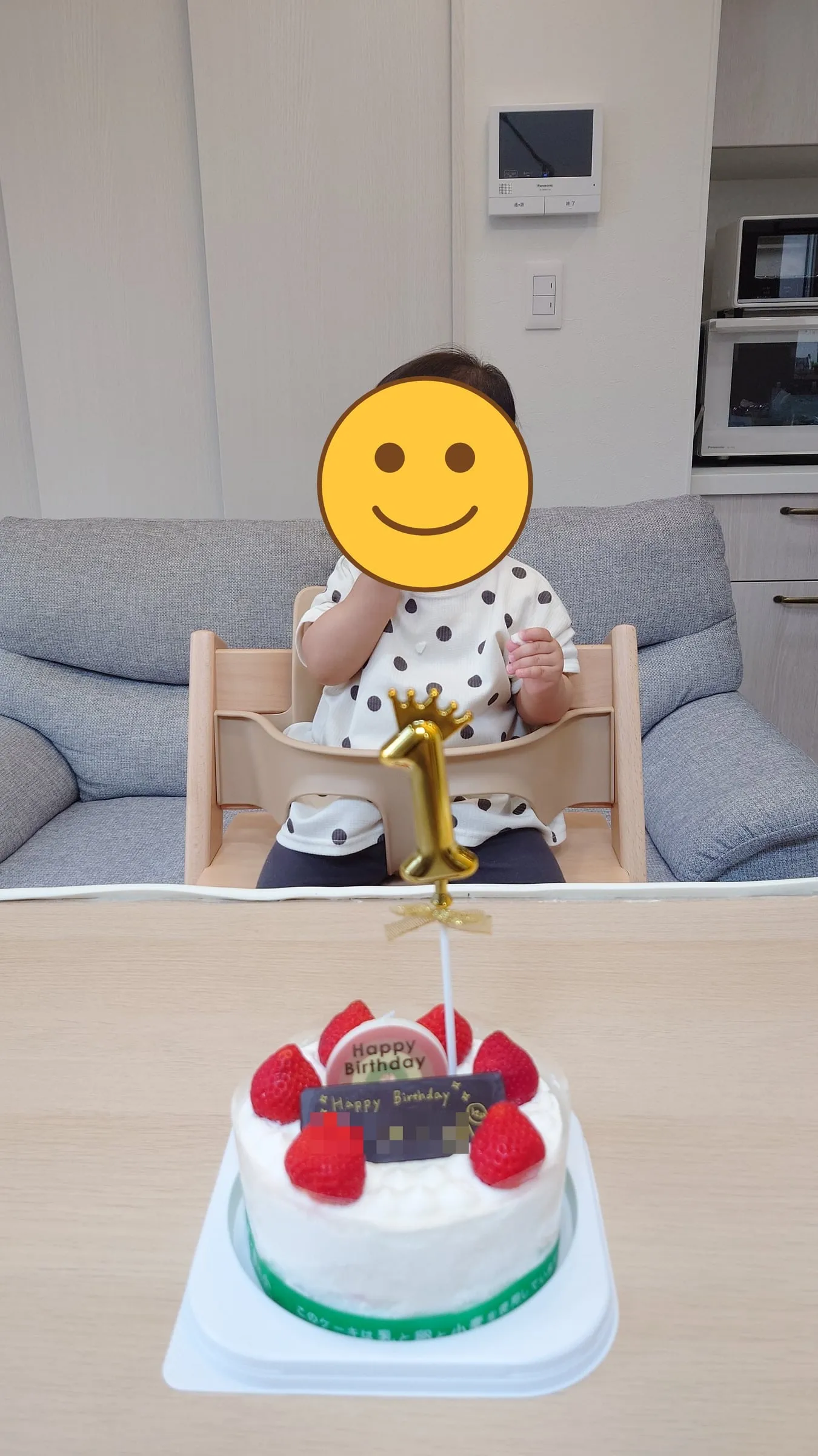 ハイチェアに座るこどもと、いちごのショートケーキ。金色の1のキャンドルが立ててある