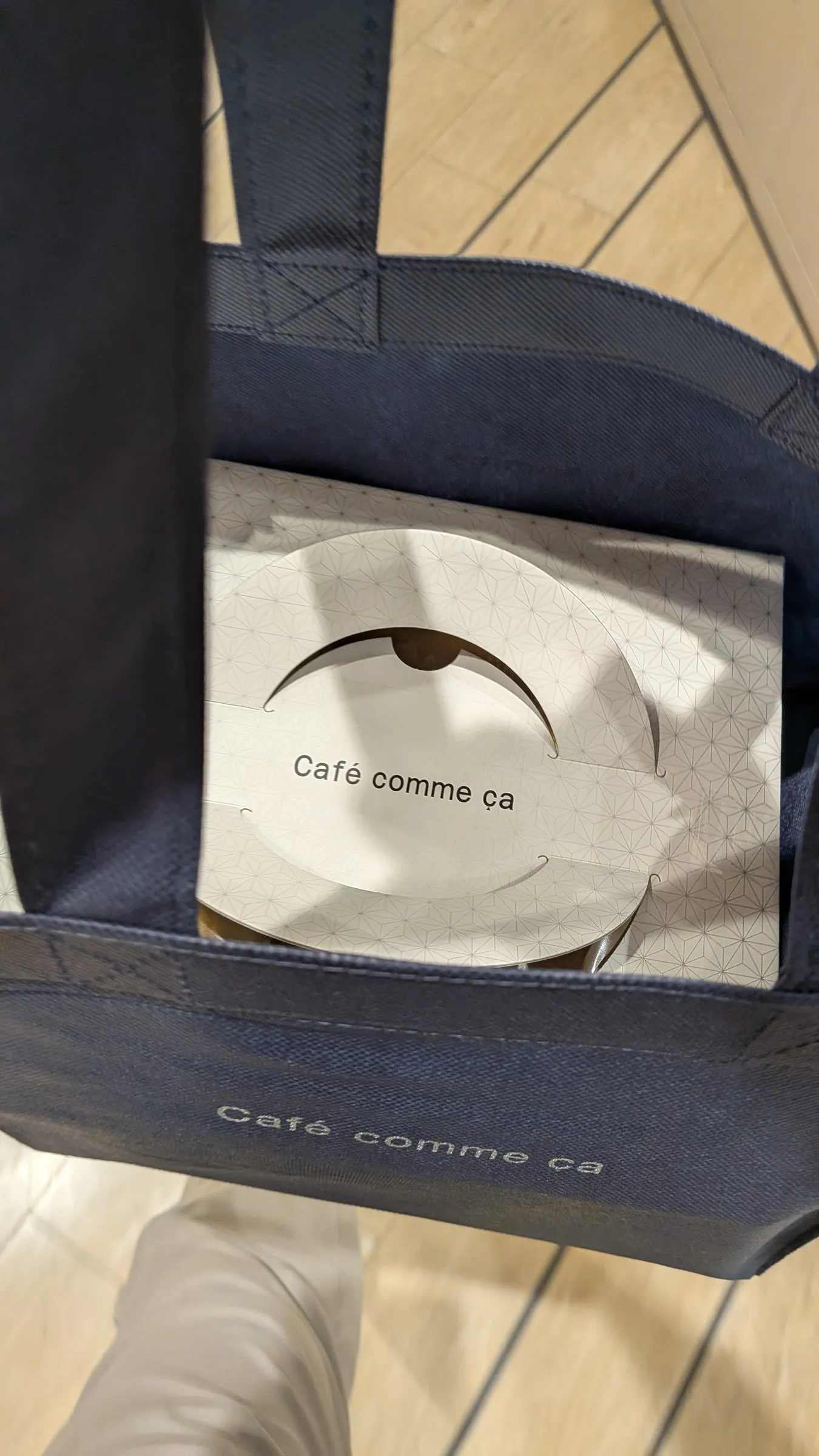 Café comme çaのロゴ入りの紺色トートバッグに、ケーキ箱が収まっている