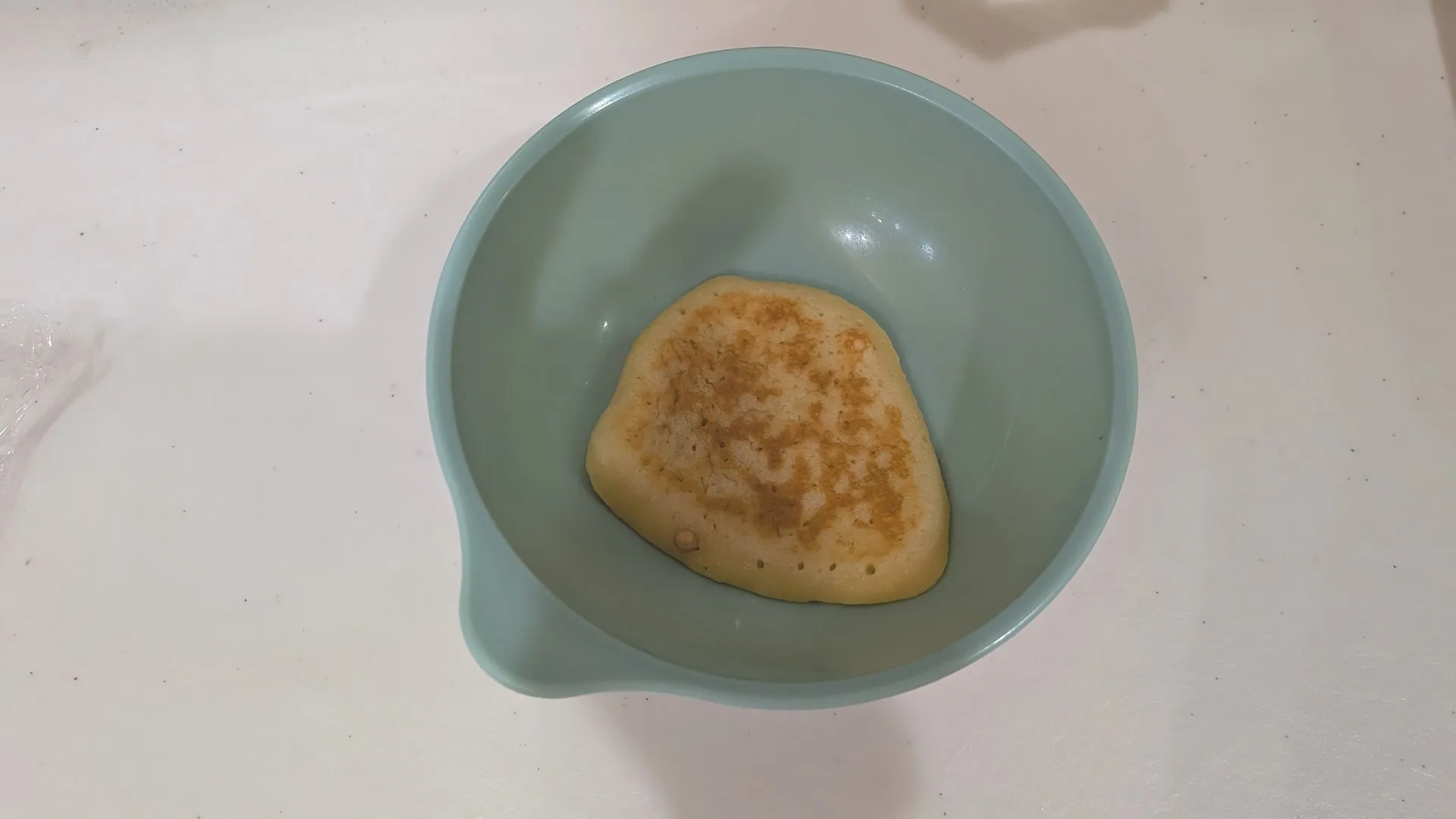 こども用の水色のボウルに入った、うっすら焼き色のついた小さなホットケーキ1枚