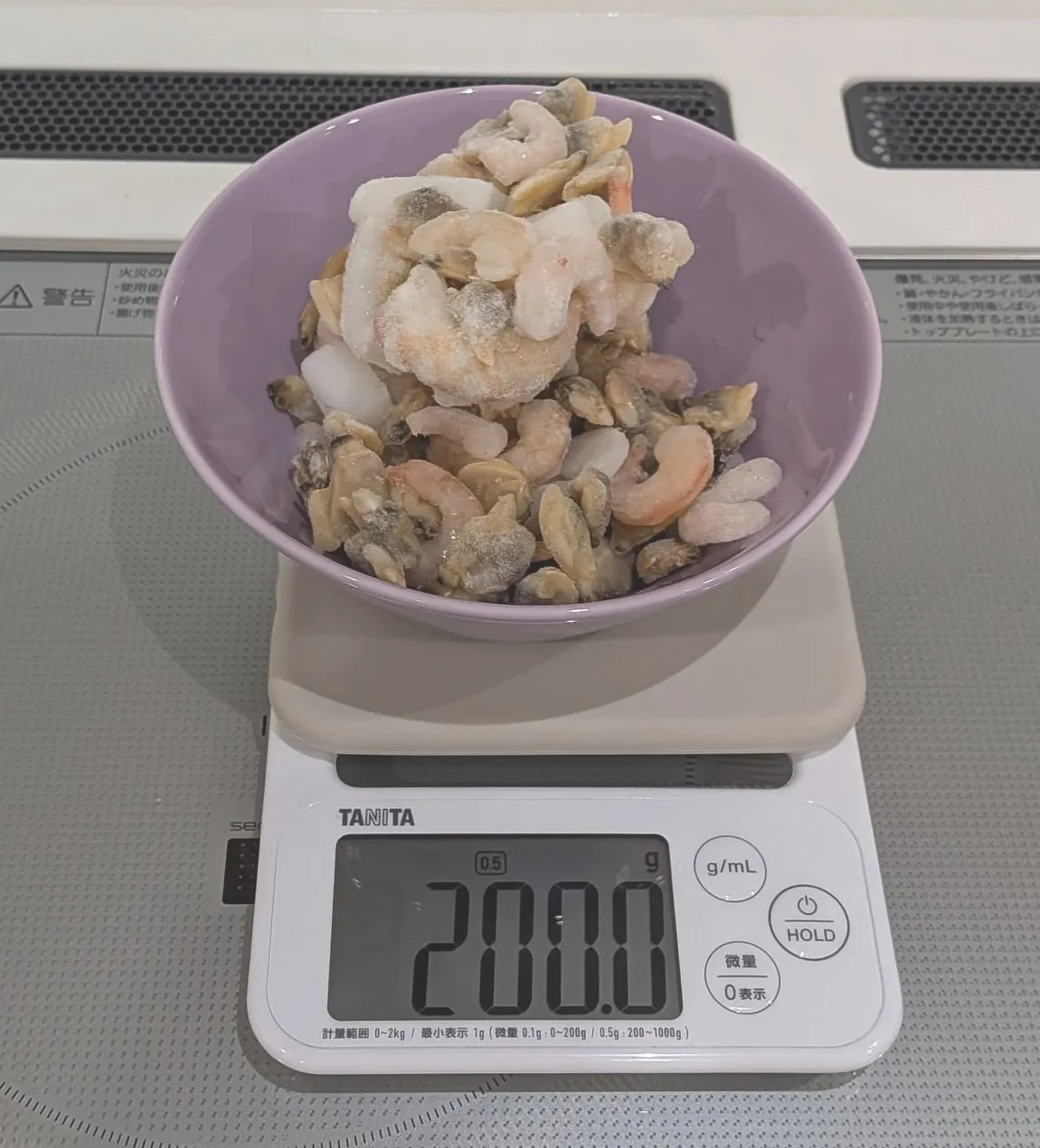 紫のボウルに入ったシーフードミックスをはかりに乗せている。表示は200.0g
